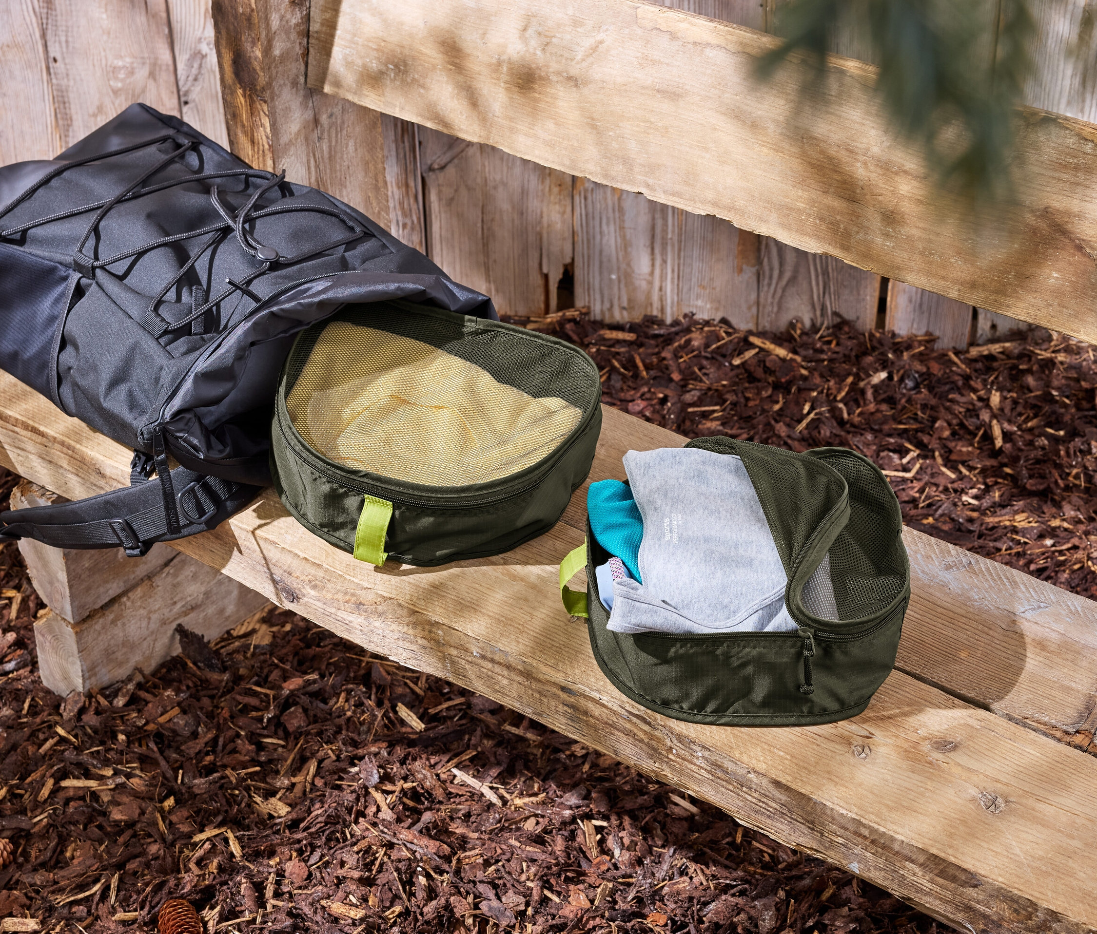 Un sac à dos noir est posé sur un banc en bois à côté de deux organisateurs de vêtements verts.