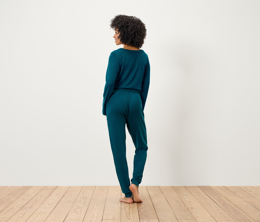 Une femme afro est vue de dos et porte un haut et un pantalon en tricot vert émeraude.