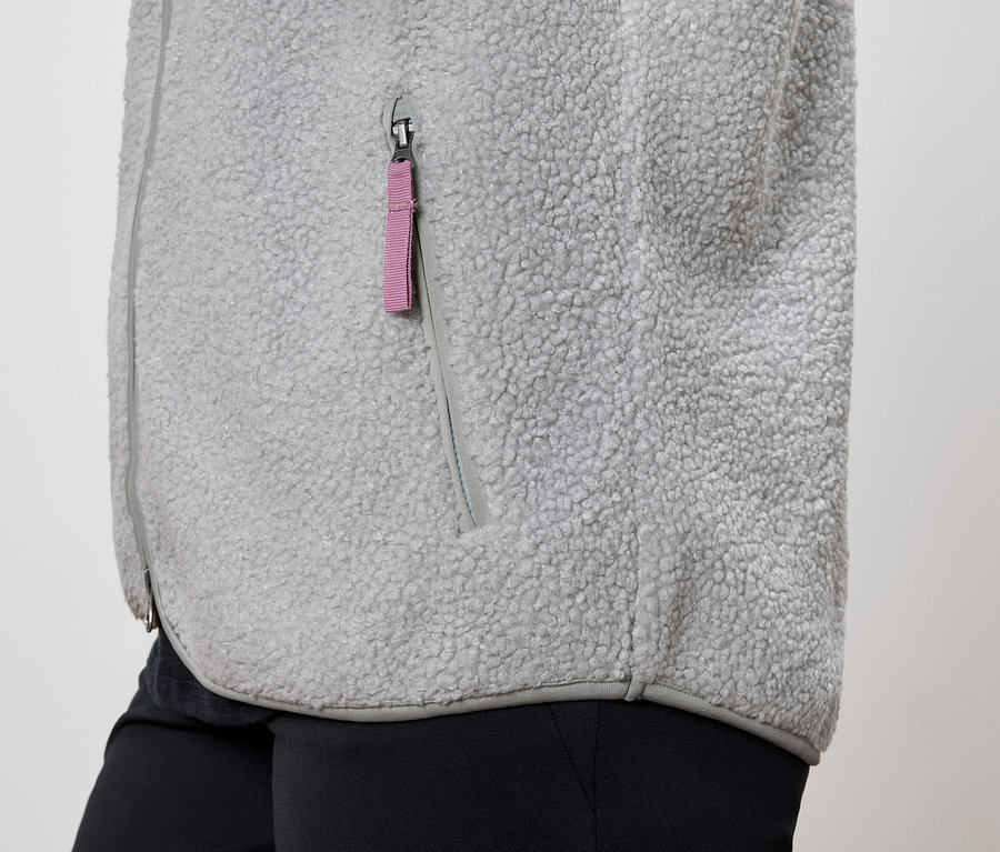 Détail d'une veste en polaire grise avec une fermeture éclair de poche rose et un pantalon noir.