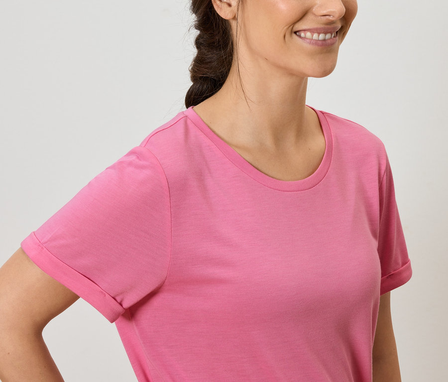 Une femme aux cheveux bruns et souriante porte un t-shirt rose.
