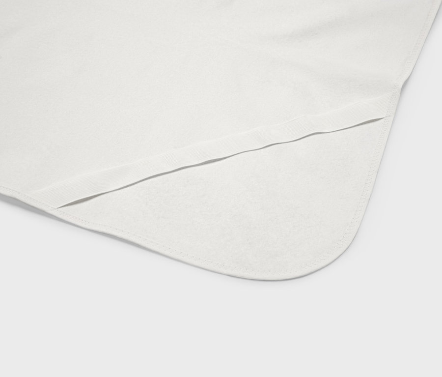 Gros plan sur une couverture de bébé blanche avec des coins arrondis et une bordure élastique.