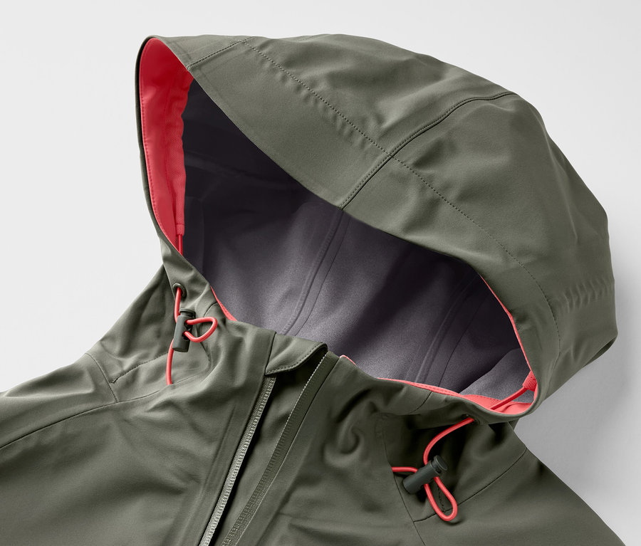 Gros plan sur une veste outdoor 3 couches verte avec capuche, doublure orange et cordon de serrage.