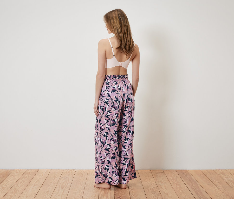 Femme vue de dos portant un soutien-gorge rose et un pantalon large à motif floral.