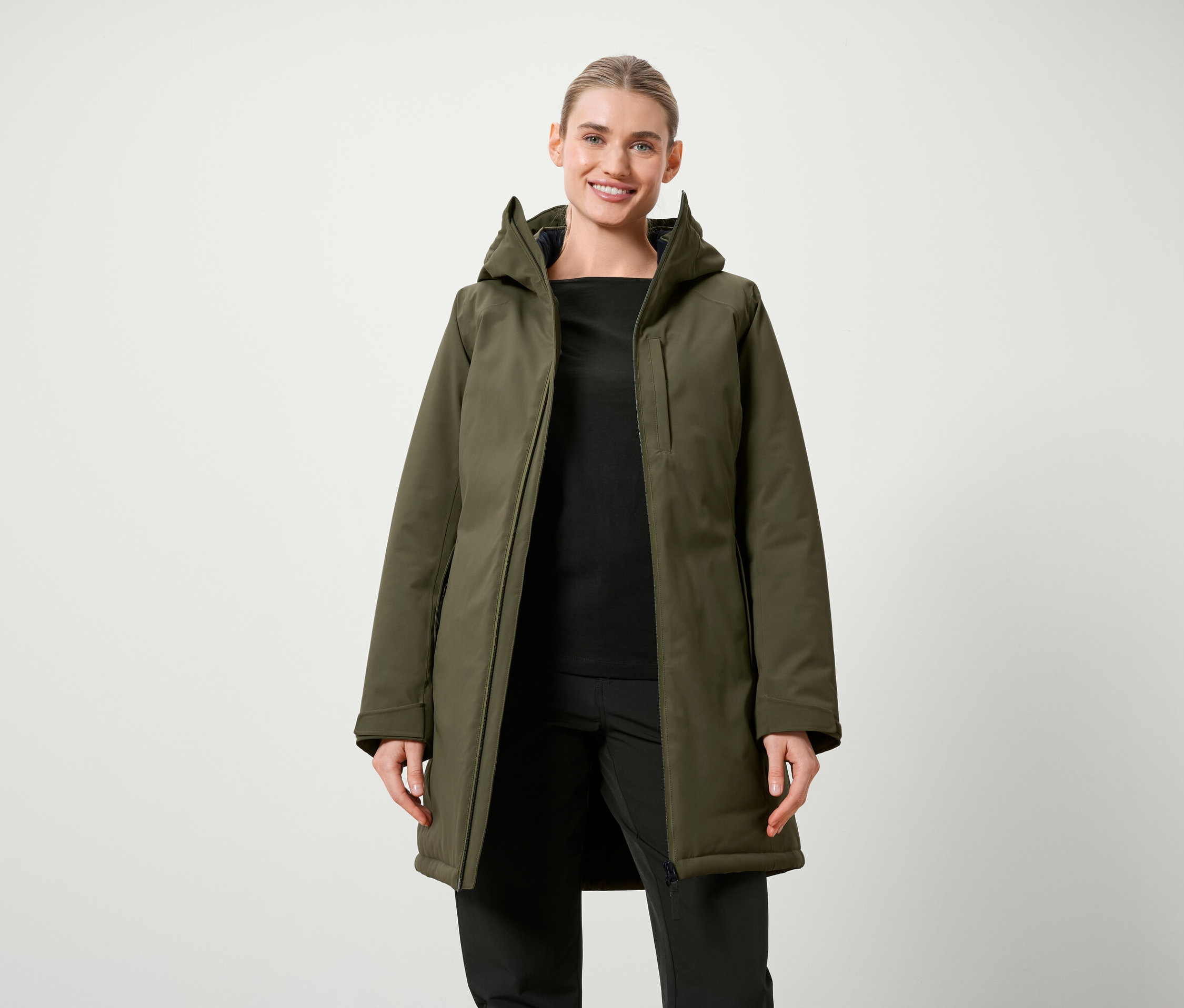 Femme posant en veste olive avec capuche et vêtements noirs.