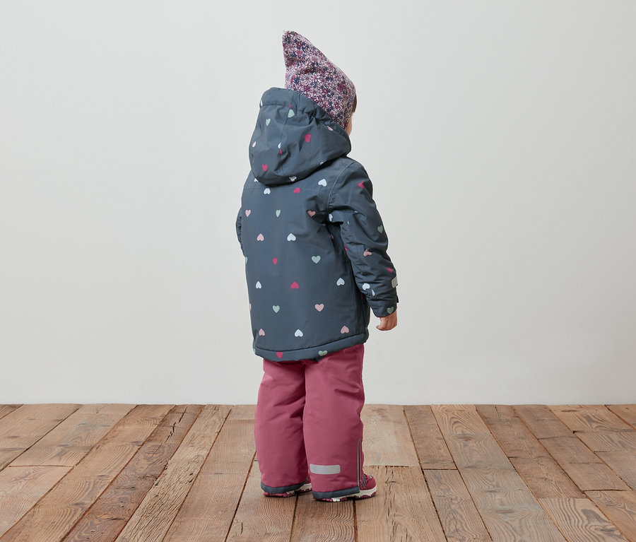 Vue arrière d'un enfant portant une veste d'hiver à capuche avec un motif de coeurs et un pantalon de neige rose.