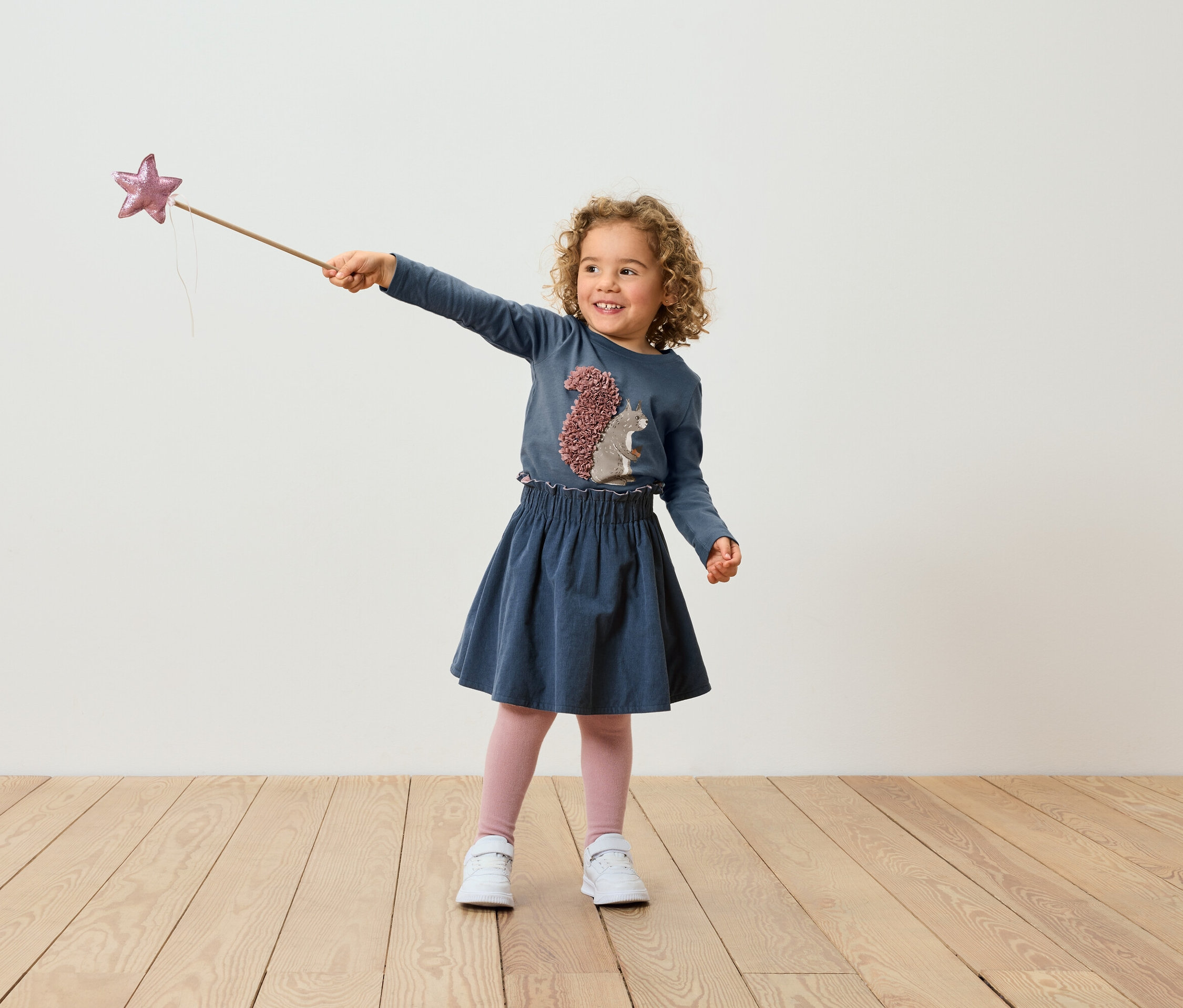 Une fillette aux cheveux bouclés, vêtue d'une robe bleue, tient une baguette magique ornée d'une étoile.