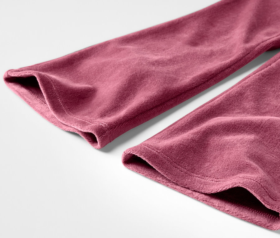 Gros plan d'un pantalon de velours bordeaux sur fond blanc.