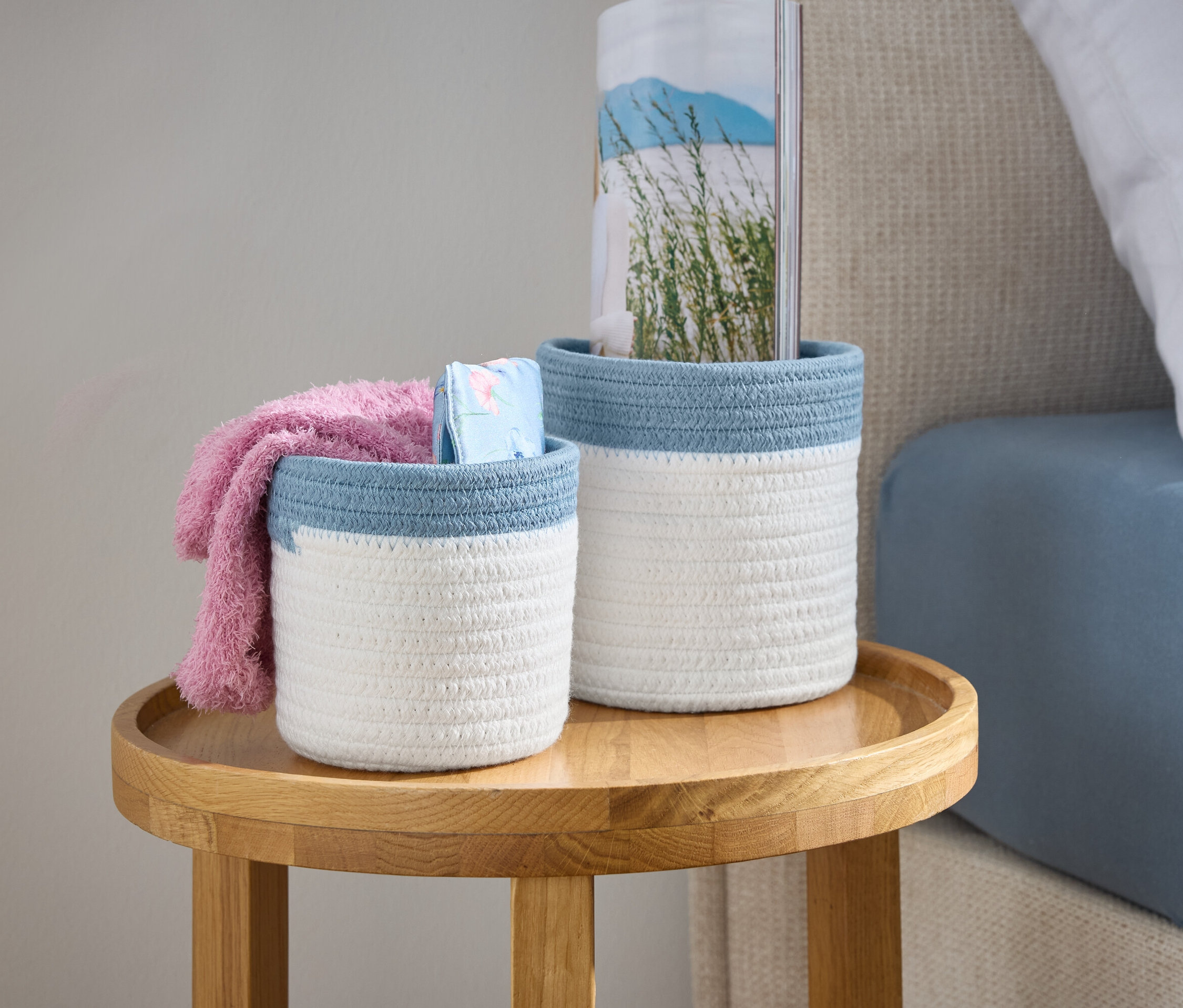 Deux paniers tressés blancs avec une bordure bleue sont posés sur une table en bois à côté d'un lit.