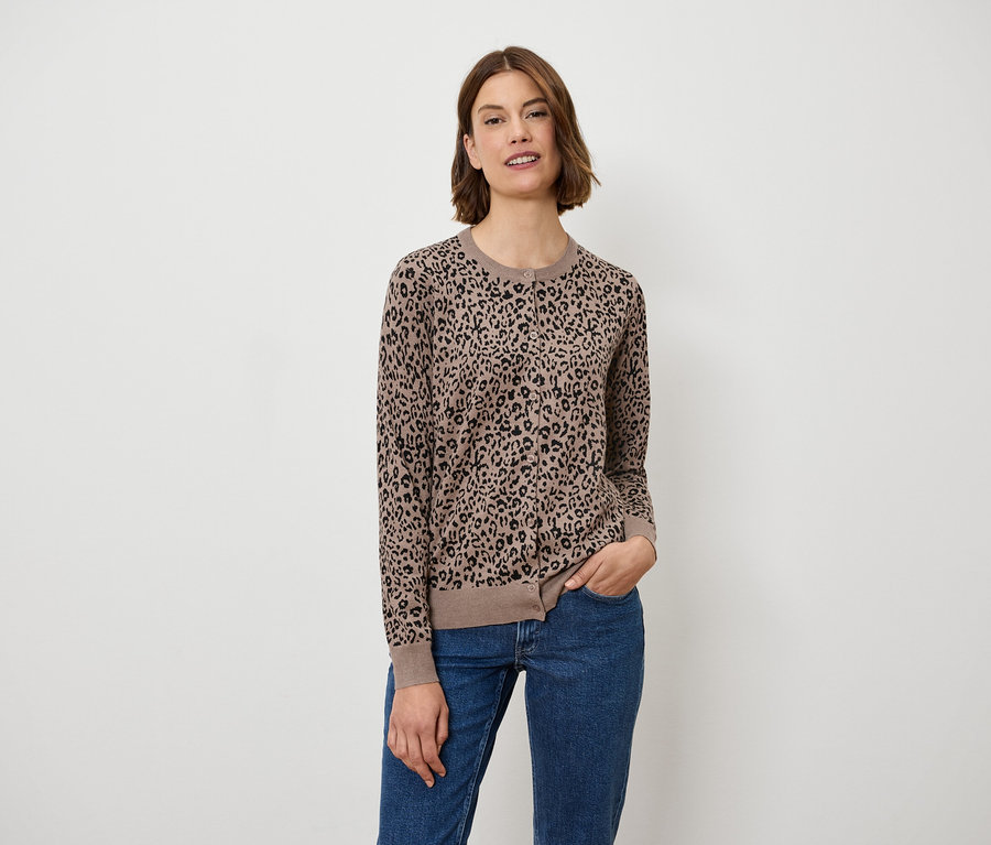 Une femme pose, portant un pull marron à motif animal et un jean bleu.