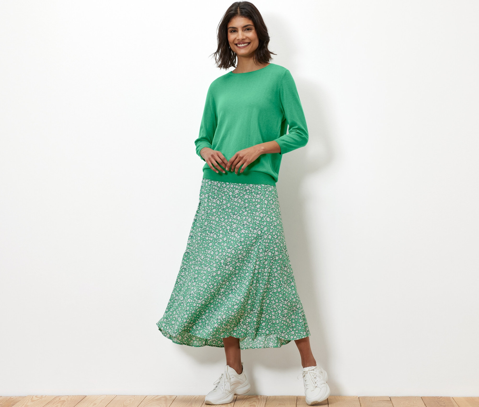 Une femme porte un pull vert en maille fine avec de la soie et une jupe à fleurs.