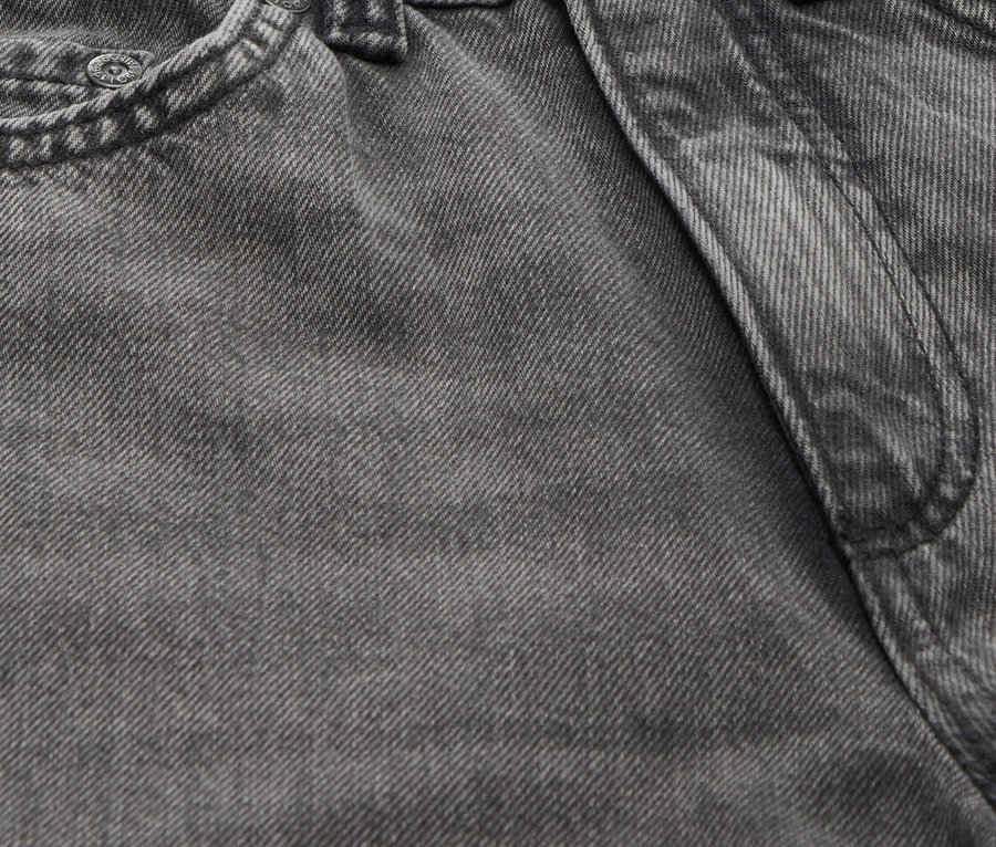 Gros plan sur un jean gris avec un bouton et des passants de ceinture.