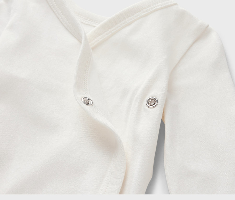 Gros plan sur un body évolutif blanc pour bébé avec des manches longues et une fermeture à bouton-pression.