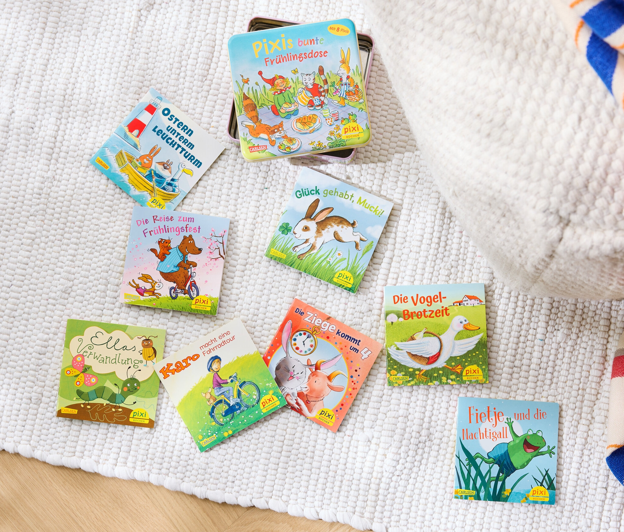 Sur un tapis blanc se trouvent un ensemble de livres « Pixis bunte Frühlingsdose » (en allemand) et d'autres livres.
