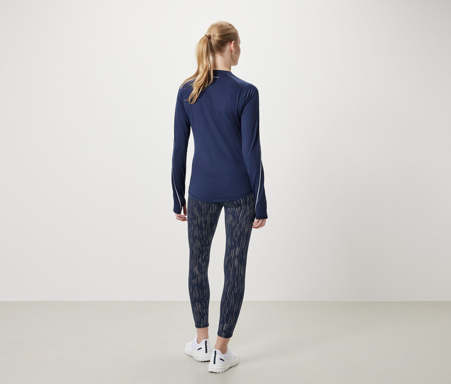 Femme portant un t-shirt de sport à manches longues bleu marine et un legging à motifs, vue de dos.
