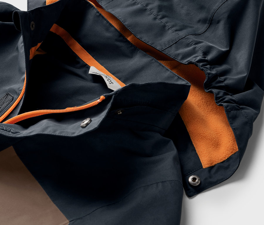 Gros plan sur une veste polyvalente pour enfant avec capuche et doublure orange.