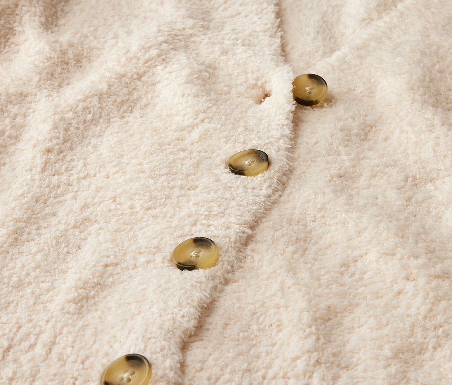 Gros plan sur un cardigan beige avec des boutons.
