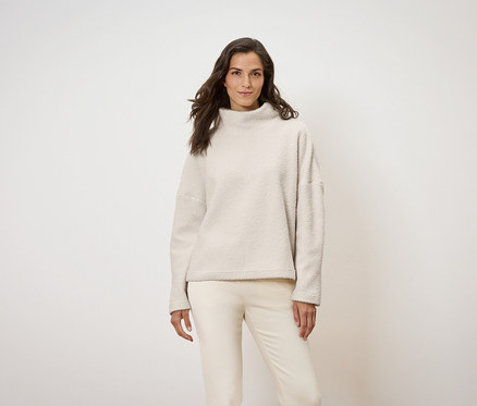 Femme posant portant un pull et un pantalon crème.