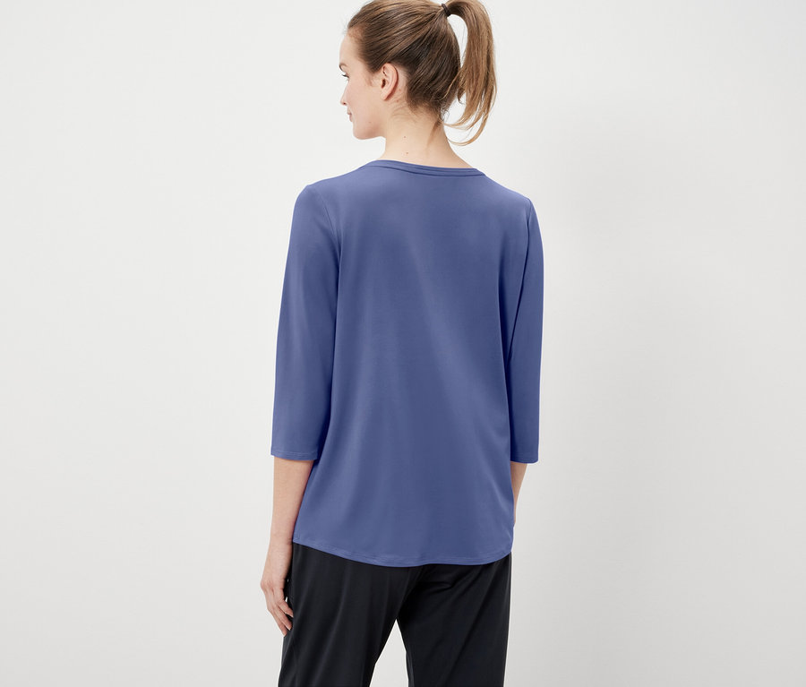 Vue arrière d'une femme aux cheveux attachés en queue de cheval, portant un t-shirt bleu à manches trois-quarts et un pantalon noir.