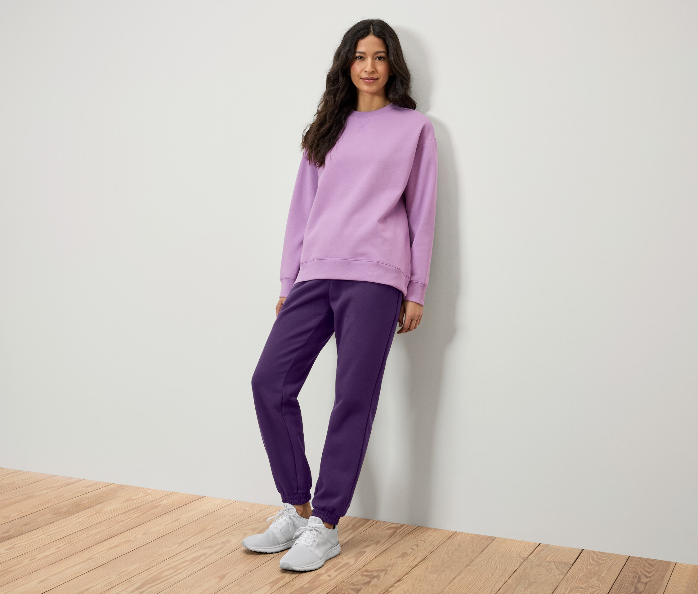 Une femme pose en sweat-shirt lilas et pantalon de jogging violet.