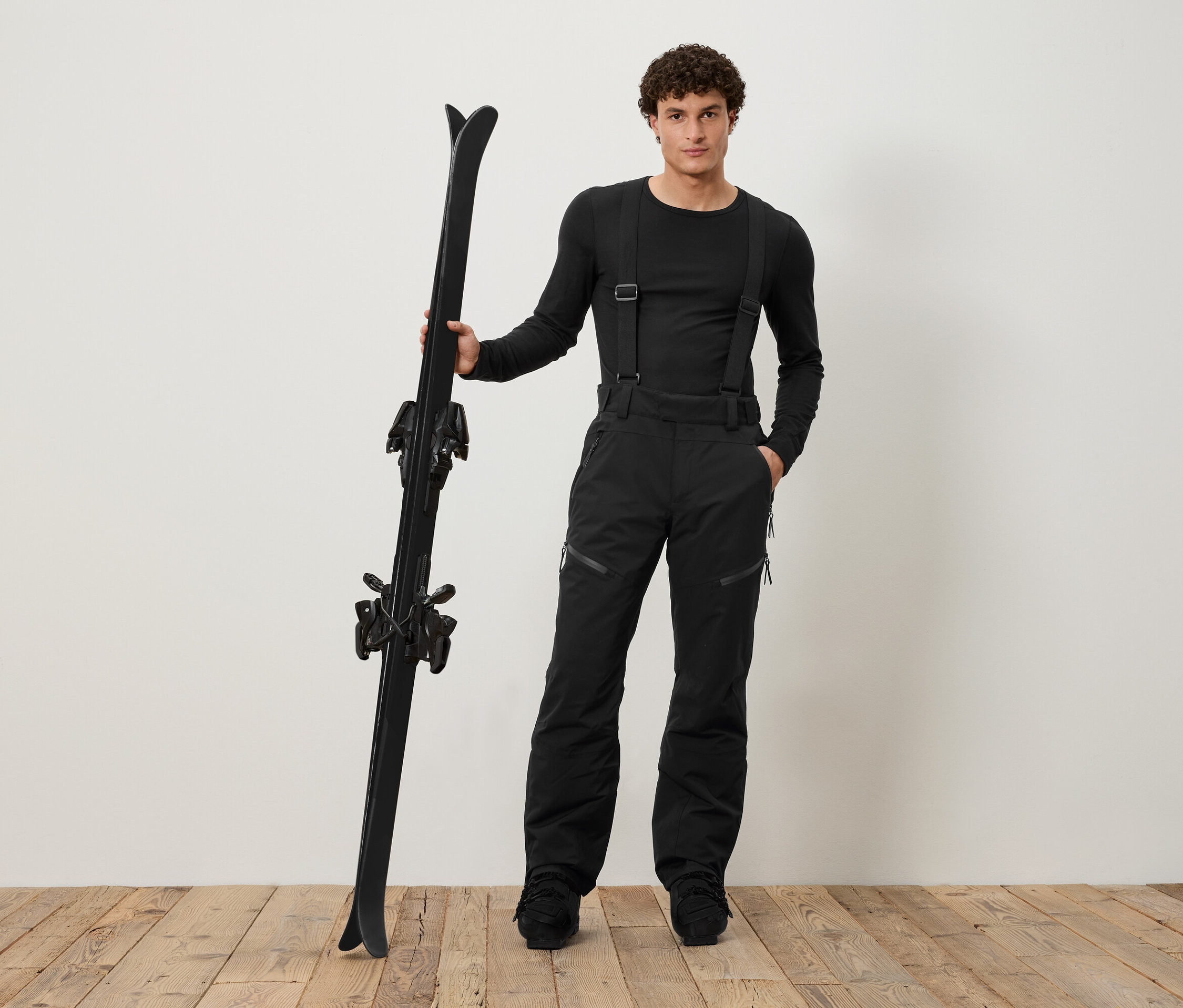 Un homme en tenue de ski noire tient des skis noirs.