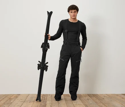 Un homme en tenue de ski noire tient des skis noirs.