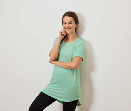 Femme portant un haut vert menthe et un legging noir, posant avec la main sur le menton.
