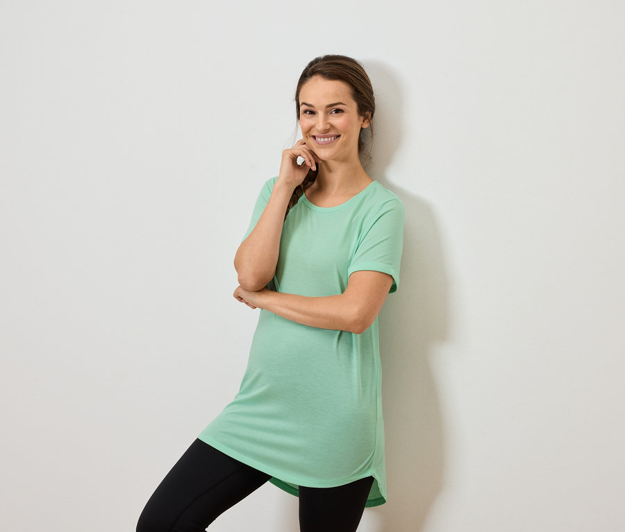 Femme portant un haut vert menthe et un legging noir, posant avec la main sur le menton.