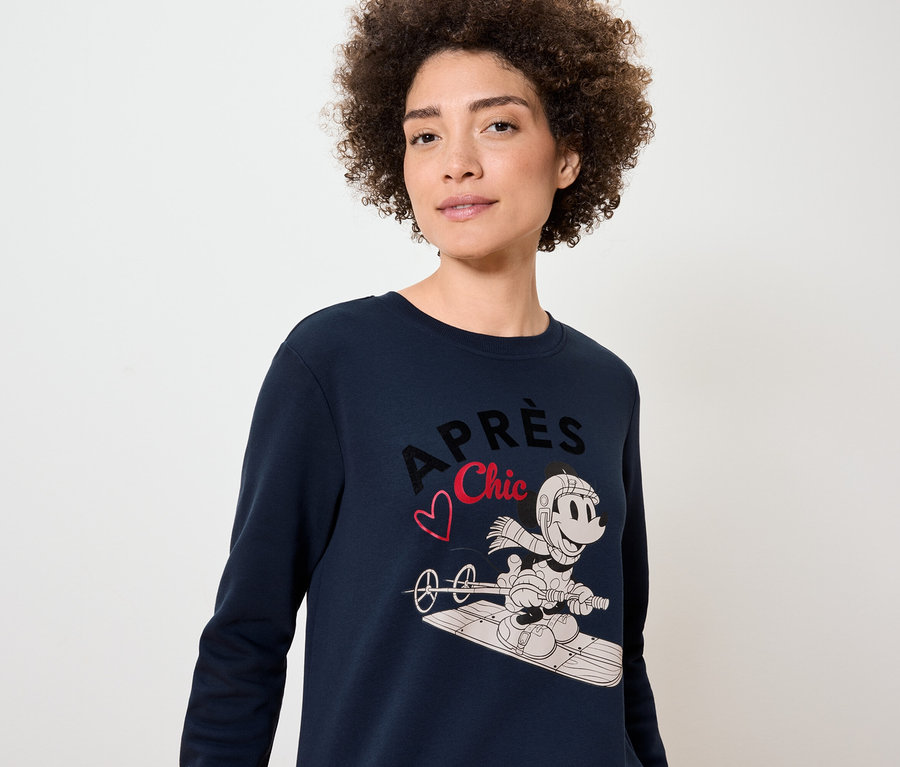Une femme porte un pull bleu marine avec un imprimé de Mickey Mouse sur un snowboard.