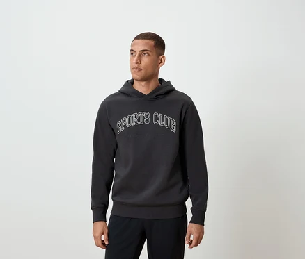 Un homme portant un sweat à capuche gris foncé avec l'inscription SPORTS CLUB.