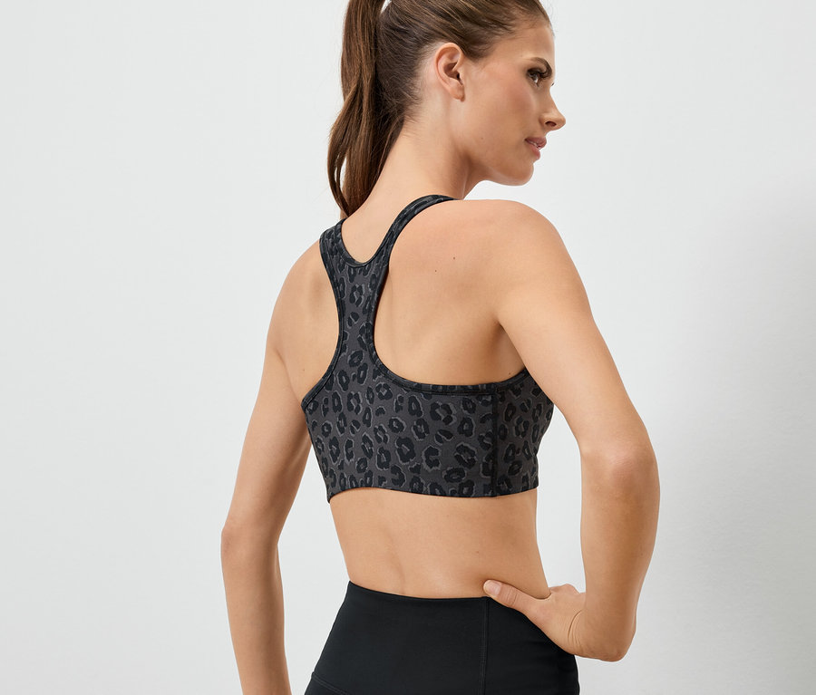 Femme dos à la caméra portant un soutien-gorge de sport à motif animalier et un legging noir.