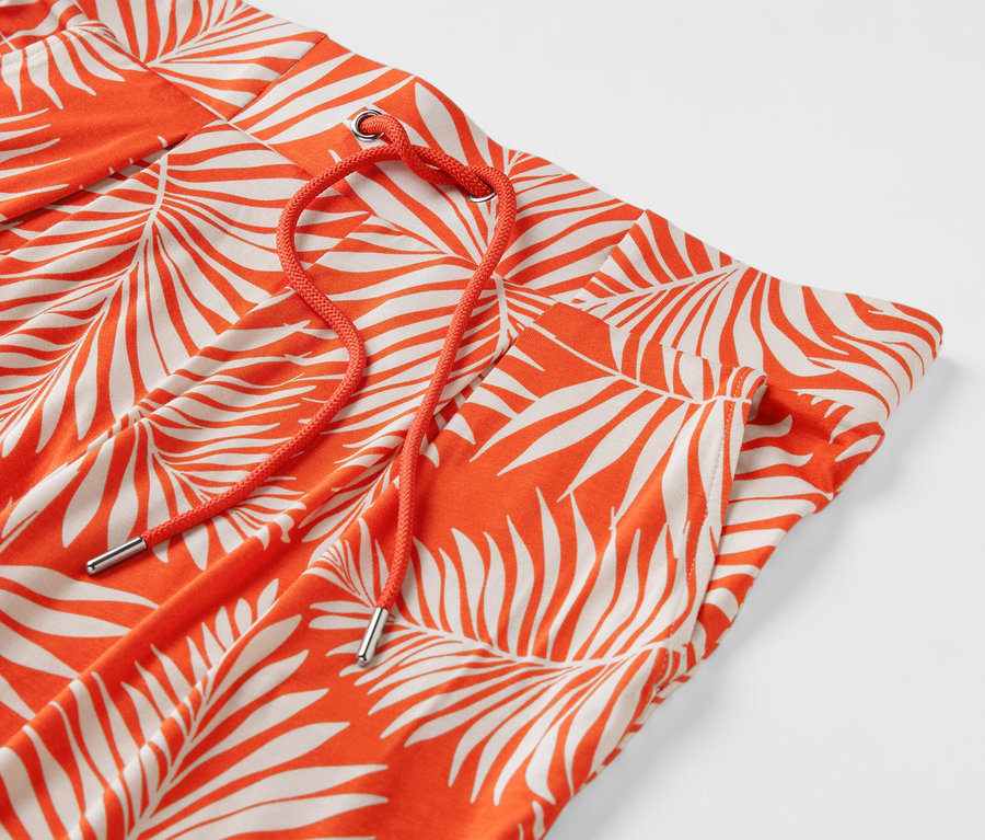 Détail d'un pantalon en jersey orange avec un imprimé de feuilles et un cordon de serrage orange.