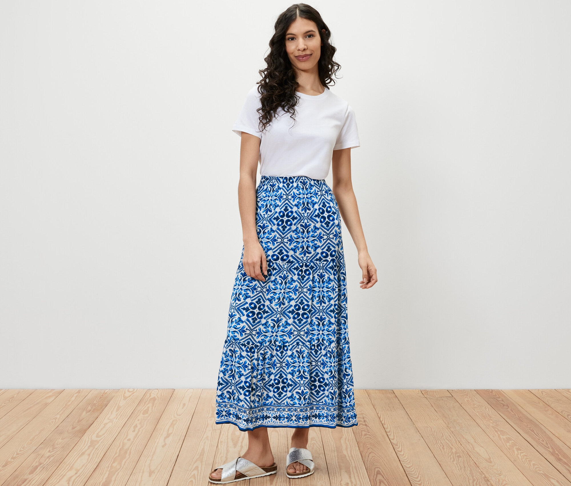 Une femme debout portant un t-shirt blanc et une jupe tissée imprimée.