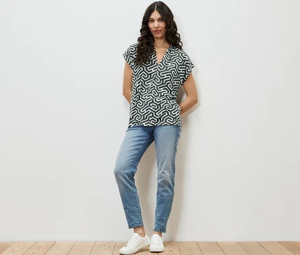 Une femme debout portant une blouse verte à encolure en V, un jean bleu et des baskets blanches.