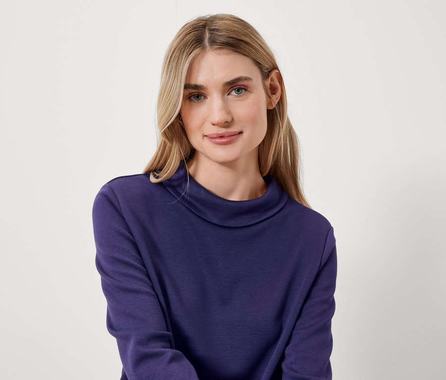 Portrait d'une femme blonde portant un pull à col roulé bleu.