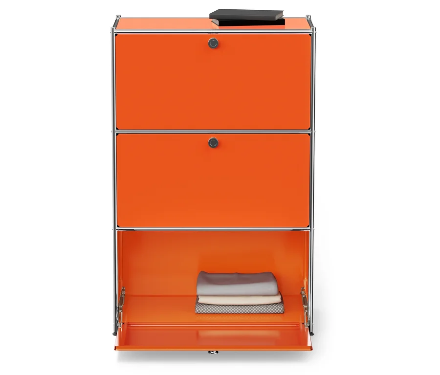 Armoire orange avec cadre argenté, la porte inférieure est ouverte et des tissus pliés sont à l'intérieur. Un livre repose sur le dessus.