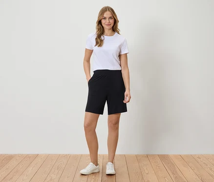 Femme portant un t-shirt blanc et un short noir debout devant un mur.