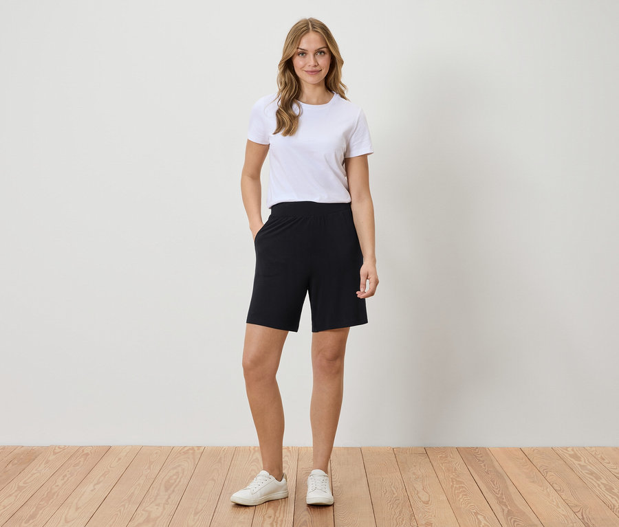 Femme portant un t-shirt blanc et un short noir debout devant un mur.