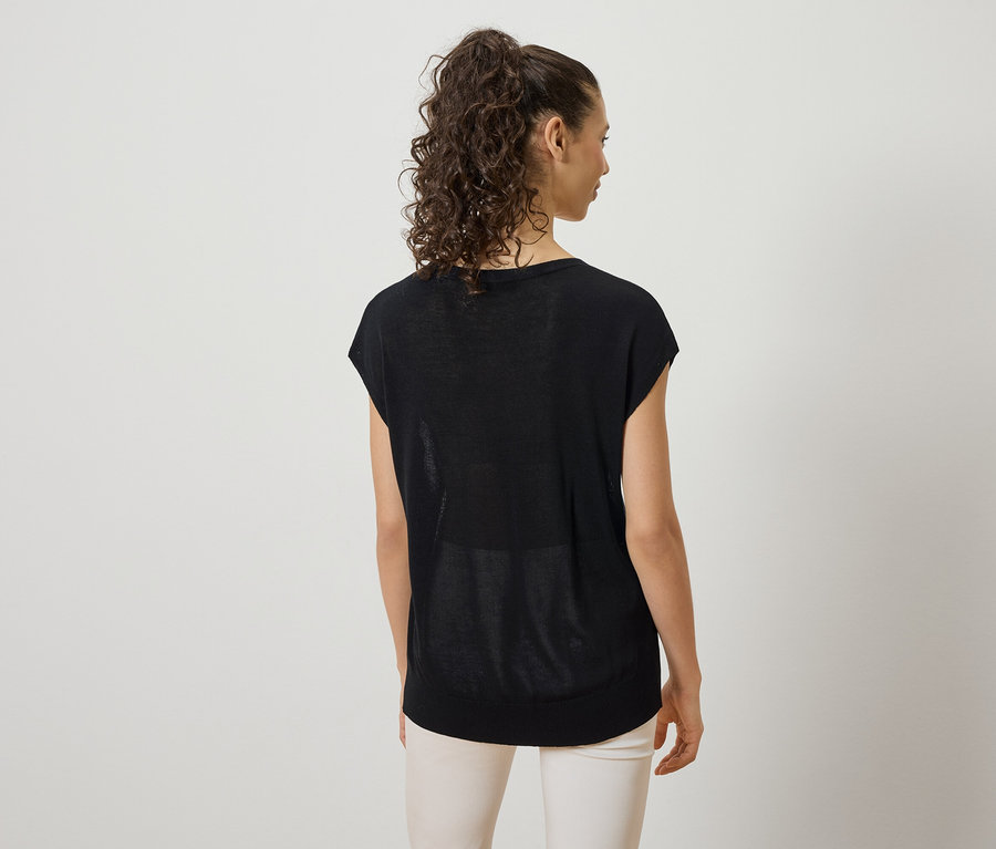 Femme aux cheveux bouclés portant un t-shirt noir et un pantalon clair, photographiée de dos.