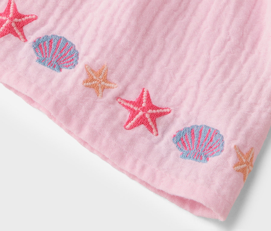 Gros plan sur un tissu rose avec des étoiles de mer roses brodées et des coquillages bleus.