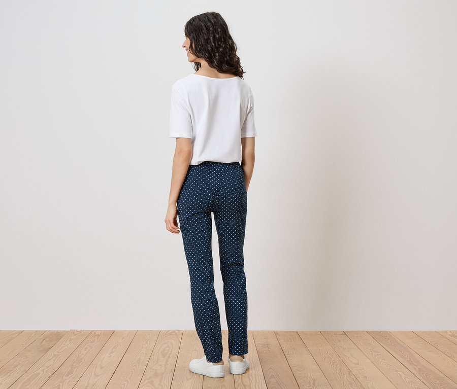 Femme vue de dos portant un pantalon bleu marine à pois blancs et un t-shirt blanc.
