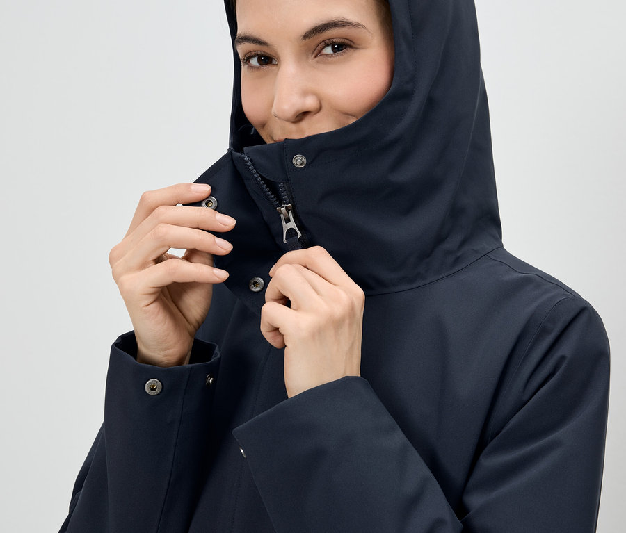 Femme fermant la fermeture éclair d'une veste à capuche bleu marine.