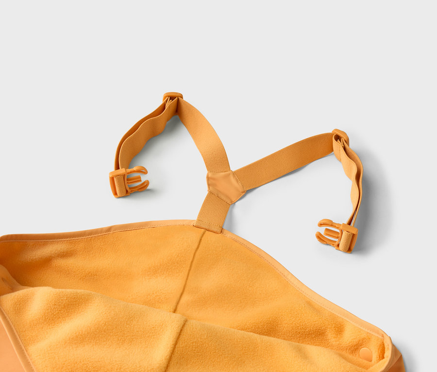 Gros plan d'une combinaison de ski jaune pour bébé avec bretelles et boucles sur fond gris.