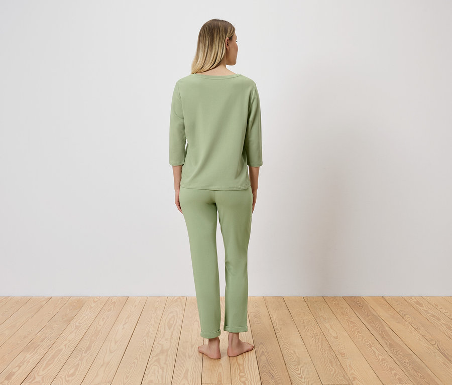Une femme blonde se tient dos au spectateur et porte un pyjama vert clair.