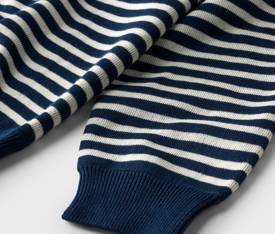 Gros plan d'un pull bleu marine à rayures blanches avec des poignets côtelés.
