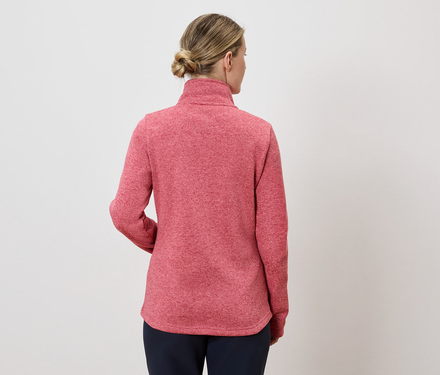 Vue arrière d'une femme blonde portant un pull rouge et un pantalon foncé sur fond blanc.
