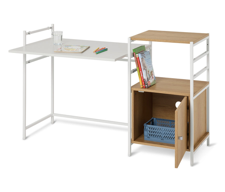 Un bureau blanc avec un verre d'eau, des crayons et un livre de coloriage dessus, à côté d'une étagère avec des livres et une boîte bleue.
