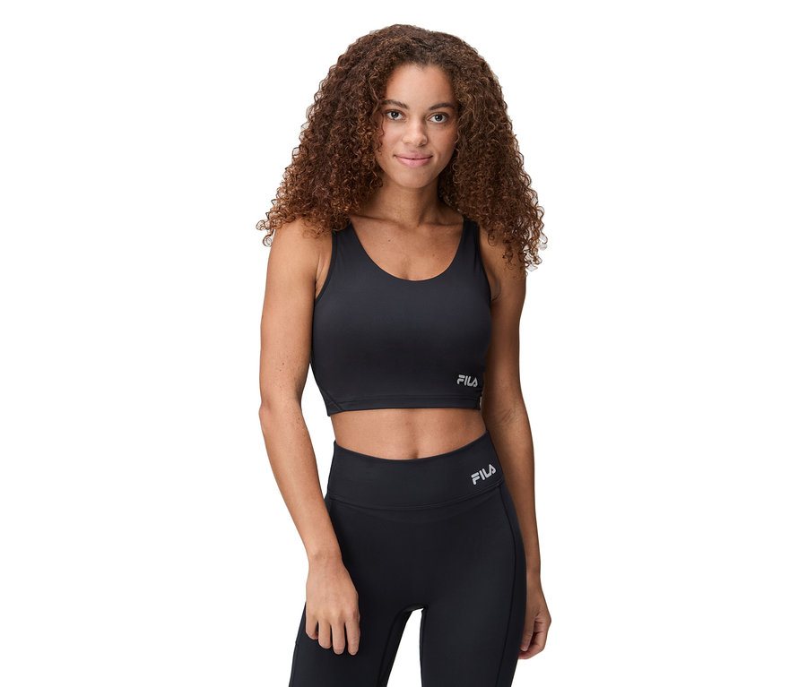 Une femme porte un soutien-gorge de sport noir et un legging avec le logo Fila.