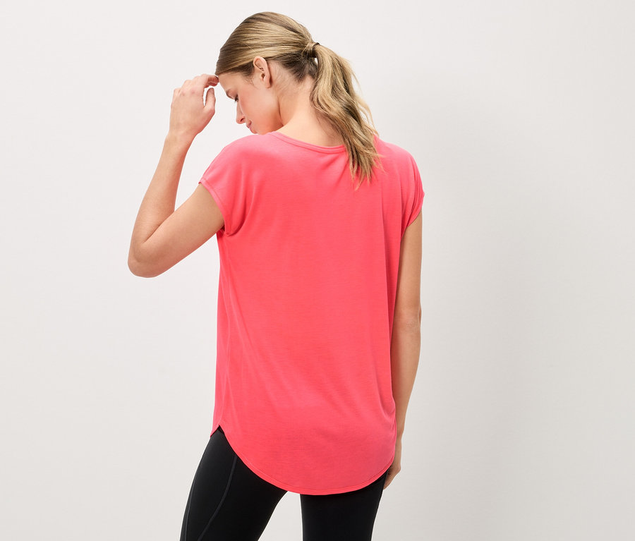 Femme vue de dos portant un t-shirt corail et des leggings noirs, touchant son front.