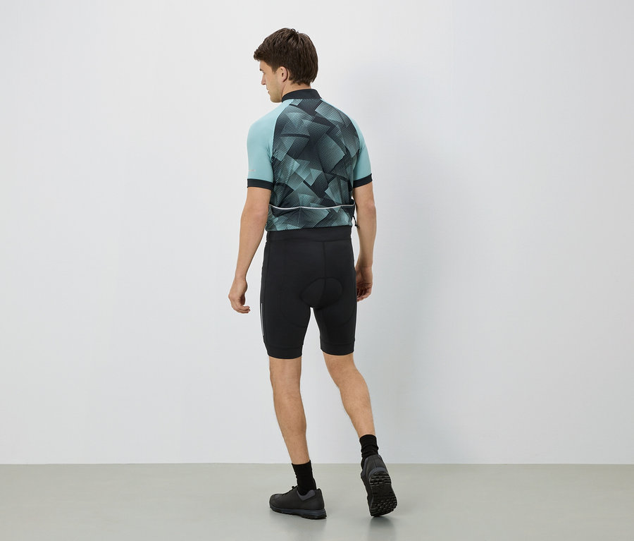 Homme de dos en tenue de cycliste, maillot bleu clair à motifs géométriques, short noir, chaussettes et chaussures noires.