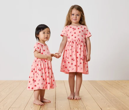 Deux filles se tiennent la main et portent des robes roses à fraises.